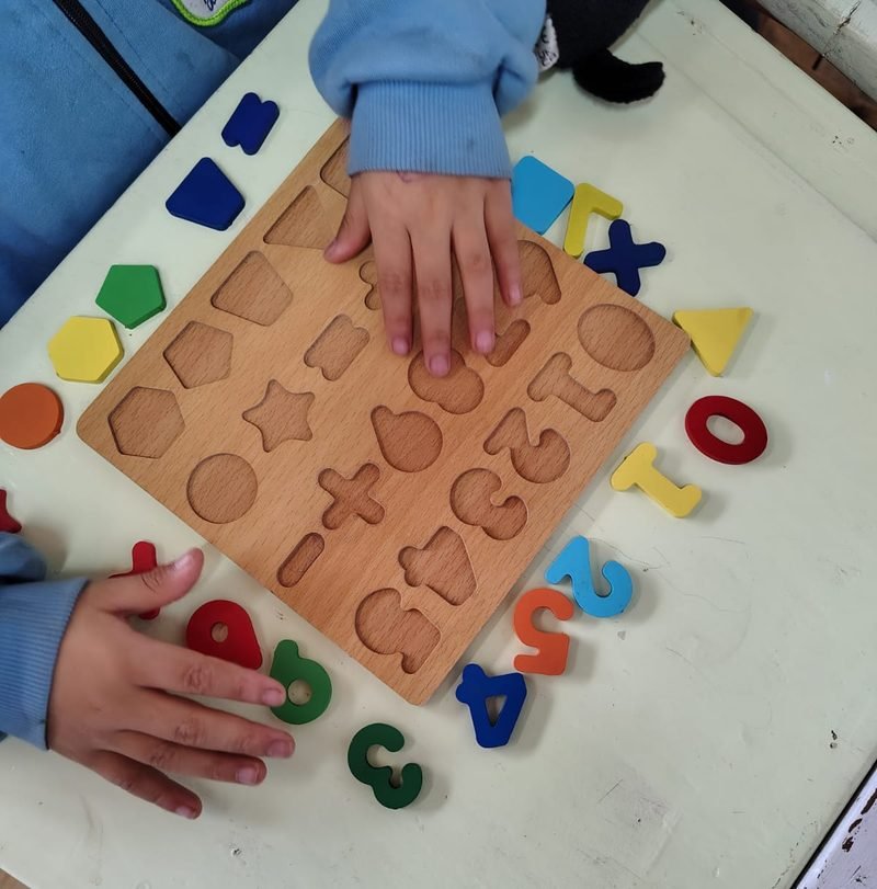 Manos de un niño que arman un encastre de madera con números y figuras de colores