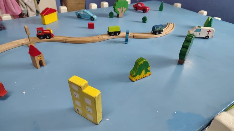 Pueblito de juguete con casitas, árboles y un tren de madera sobre una mesa celeste